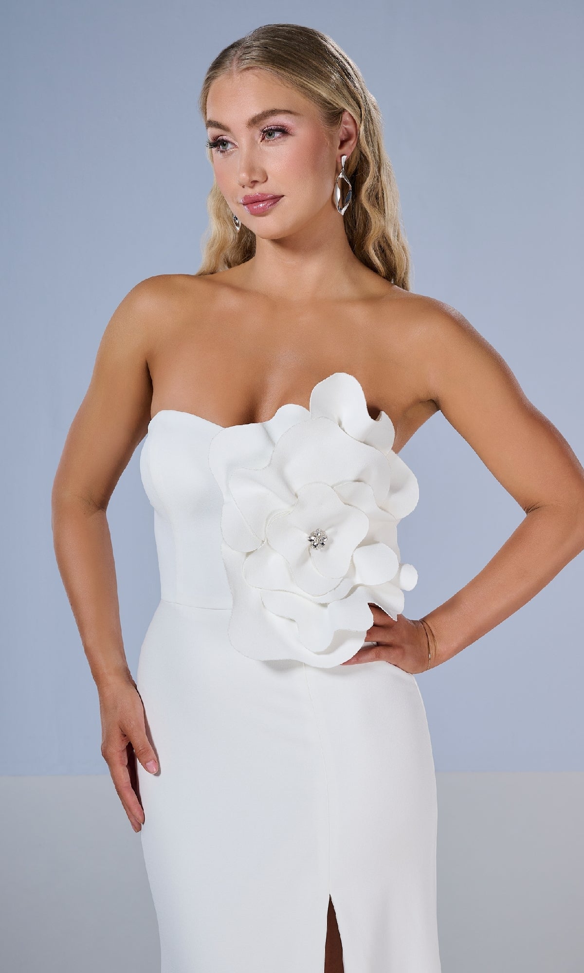 Woman models the Tiffany 16222 long prom dress, featuring a strapless design, 3D floral details, and a thigh-high slit. She poses confidently with one hand on her hip against a plain background.